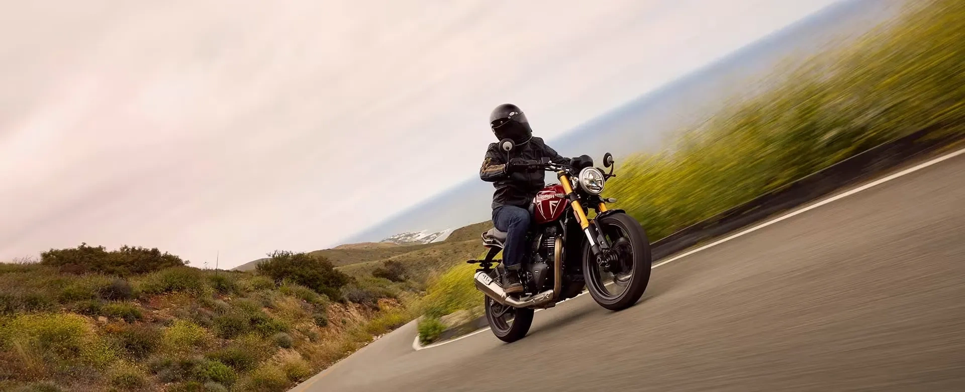 Triumph Speed 400 rouge en conduite dynamique sur une route panoramique.