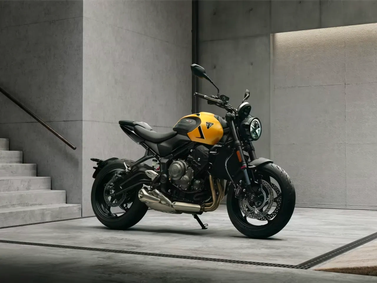 Triumph Trident 660 jaune stationnée près d’un escalier en béton.