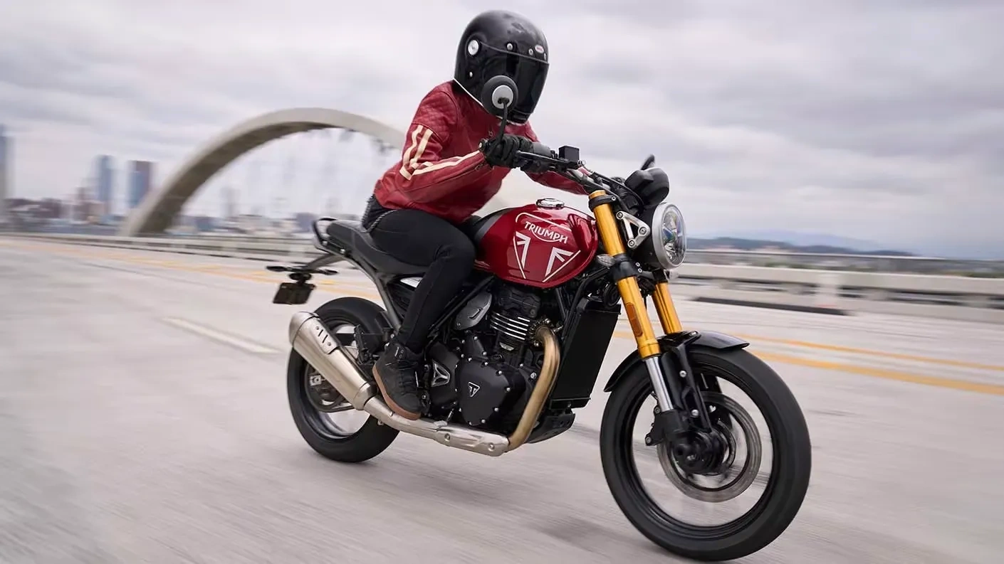 Motocycliste au guidon d’une Triumph Speed 400 rouge sur un pont.