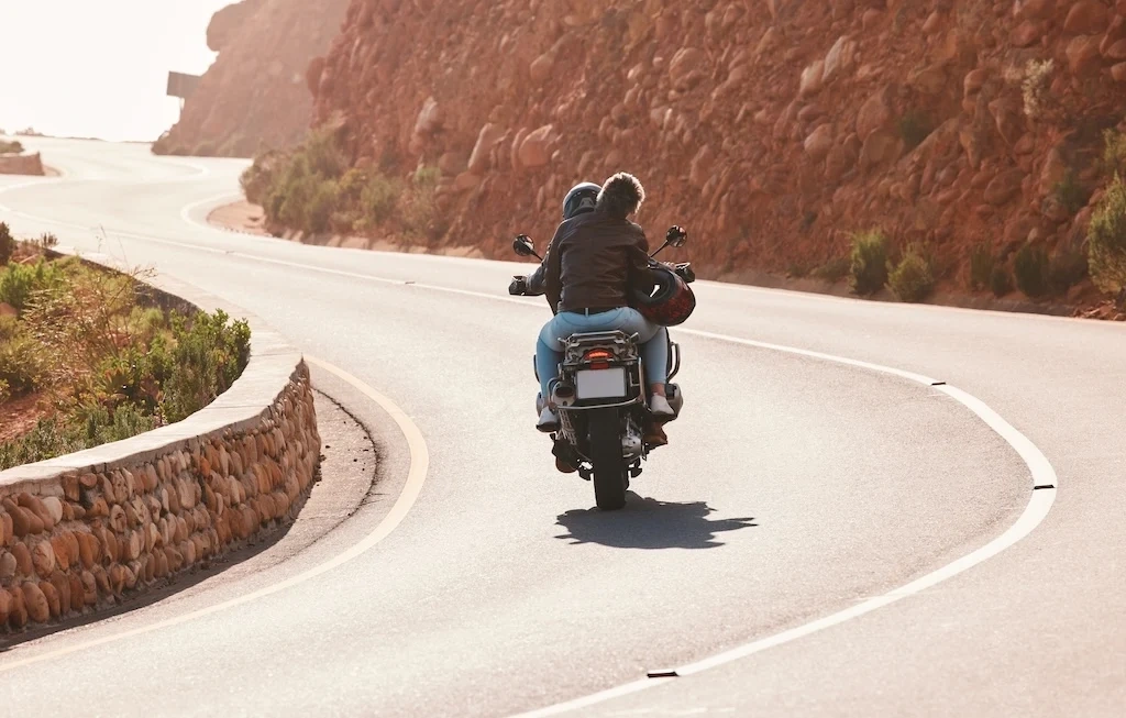 Moto de tourisme avec passager sur une route sinueuse, idéale pour voyager à deux.