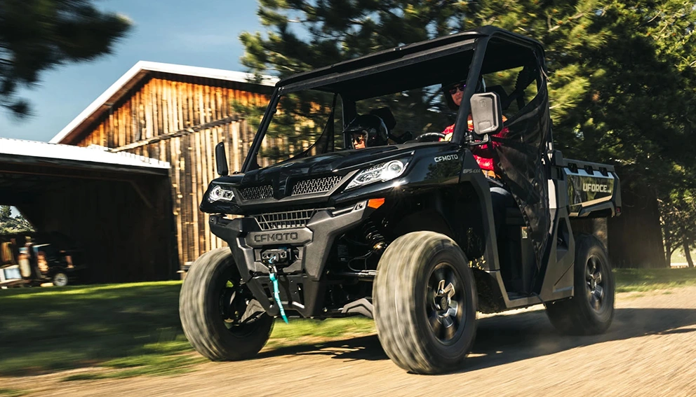 CFMoto UForce 1000 2026 noir circulant devant une grange en bois, allée ensoleillée.