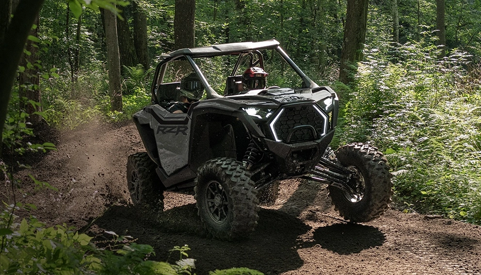 Polaris RZR PRO XP 4 Sport noir en pleine action sur sentier boisé, projetant de la terre en dérapage.
