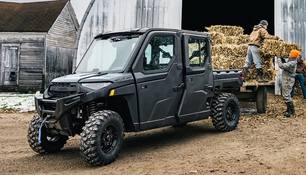 Polaris Ranger 1000 XP NorthStar 2026 gris foncé garé dans une ferme, avec des travailleurs chargeant des balles de foin en arrière-plan.