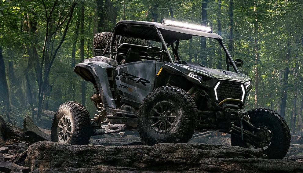 Polaris RZR XP franchissant des rochers en forêt brumeuse.