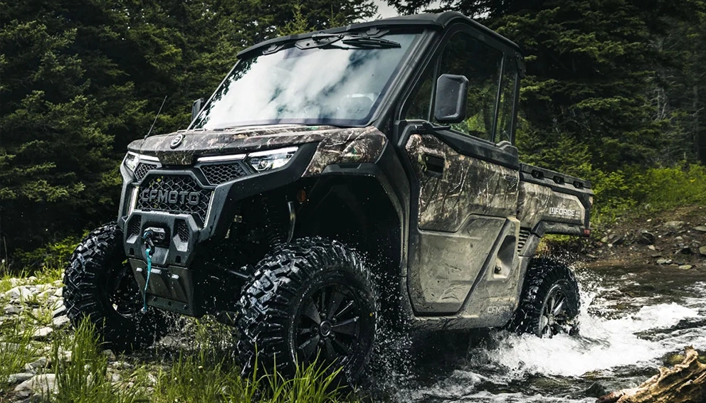 CFMoto UForce U10 Pro Highland 2026 en camouflage traversant un ruisseau en forêt.