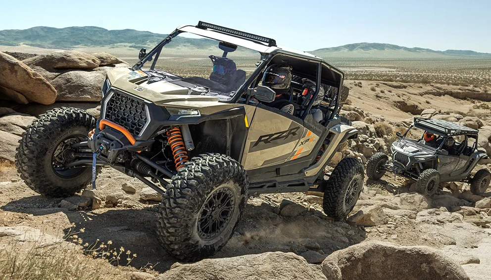 Polaris RZR Pro XP 2026 beige franchissant un terrain rocailleux désertique, un second véhicule visible en arrière-plan.