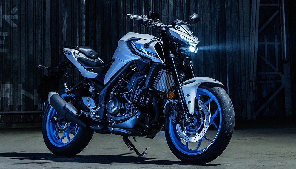 Yamaha MT-03 en arrêt dans une cour industrielle avec phares allumés 
