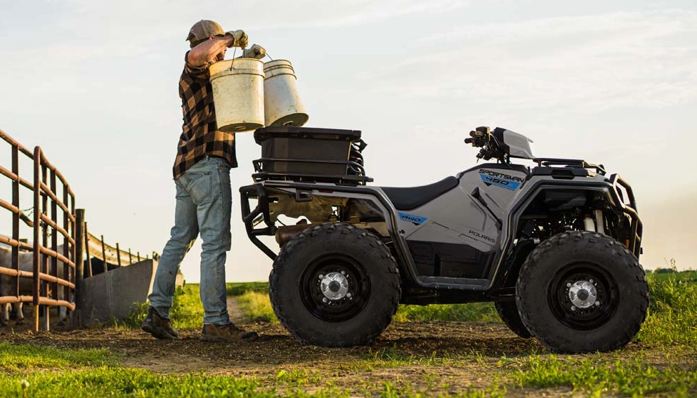 View of the Polaris Sportsman 450 Utility HO and a man loading two buckets of rocks onto the ATV