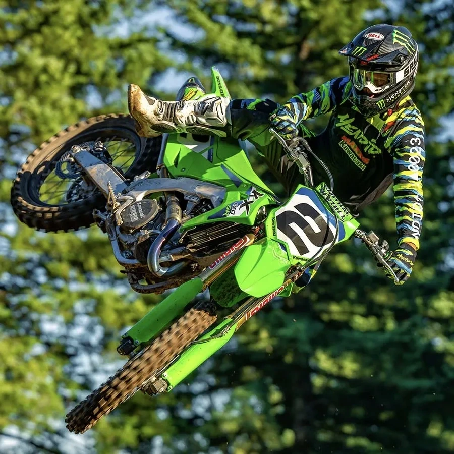 Kawasaki KX450SR verte sautant sur un sentier de motocross en forêt.