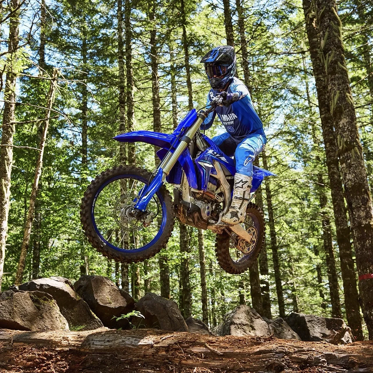 Yamaha YZ450FX bleue sautant sur un sentier de motocross en forêt.