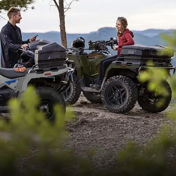 Deux personnes photographiant un Polaris Sportsman 570 en forêt.