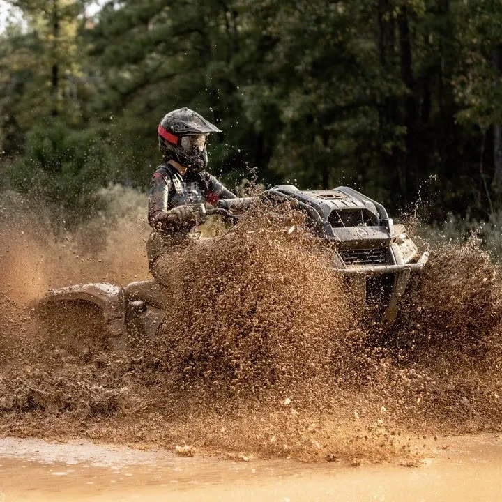 Can-Am Outlander 500 en conduite dans la boue en forêt.