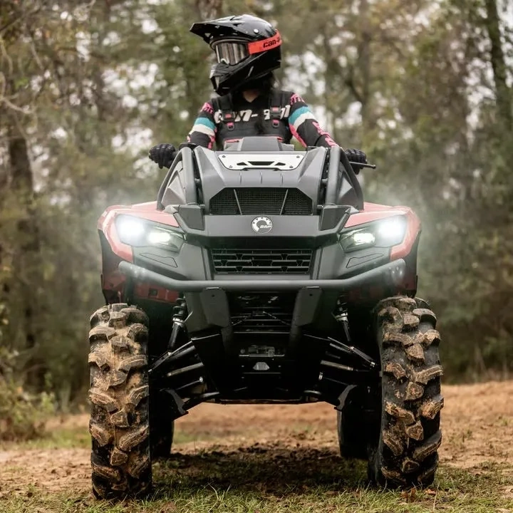 Can-Am Outlander 500 en conduite en forêt, phares allumés.