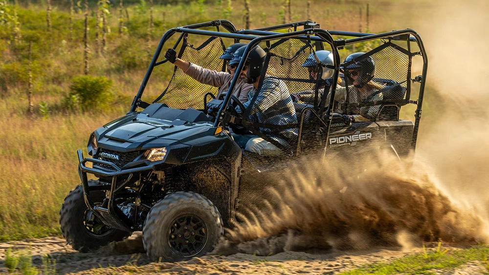 Vue de deux couples d'amis dans un Honda Pioneer 700-4 en pleine puissance sur chemin de sable