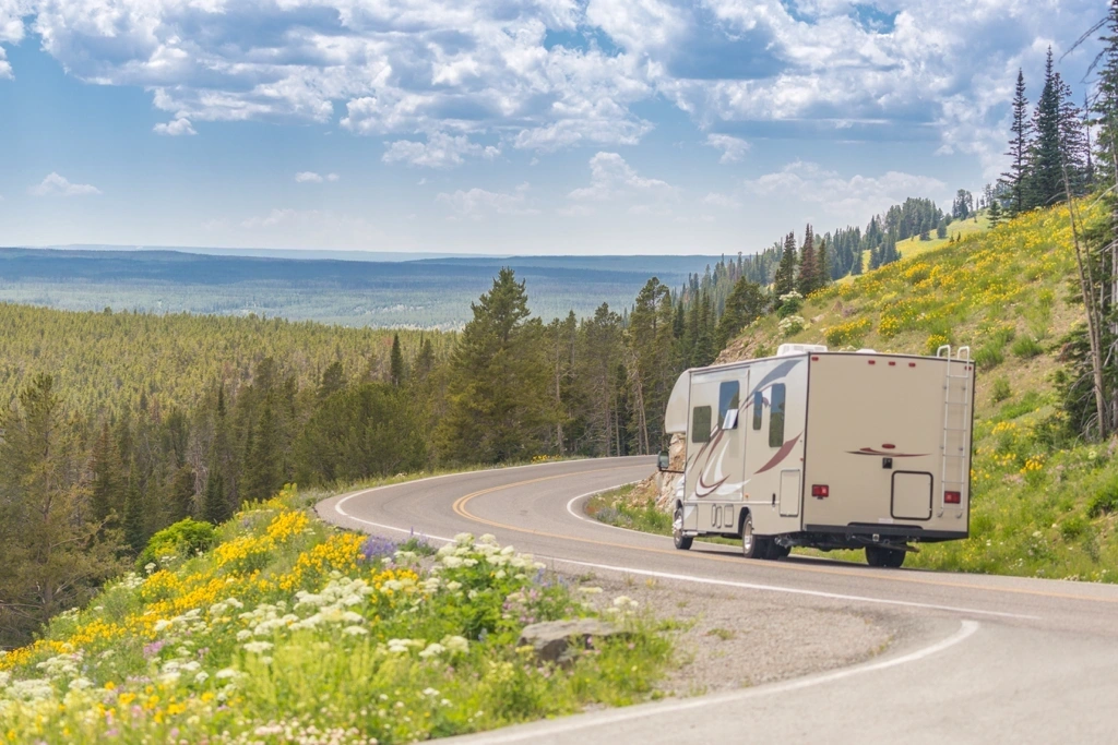 Roulotte roulant sur une route de montagne bordée de fleurs sauvages et de conifères, illustrant la planification d’un voyage en VR et l’estimation du budget selon la roulotte.