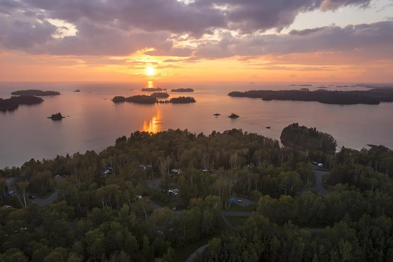 Vue aérienne au coucher du soleil du parc national de la Pointe-Taillon, montrant les îles du lac Saint-Jean, la forêt dense et les emplacements de camping en bordure de l’eau.