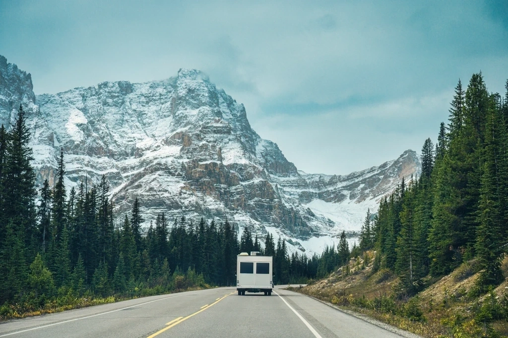 VR roulant sur une route des Rocheuses bordée de montagnes enneigées, illustrant la majesté du paysage albertain.