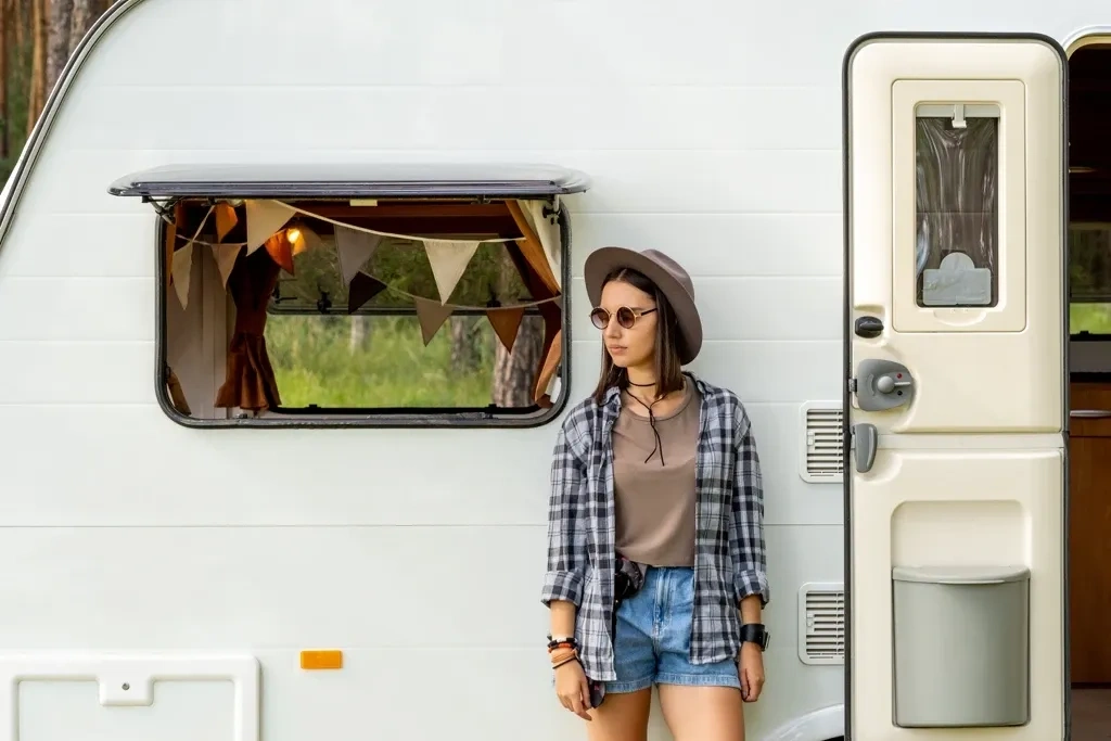 Jeune femme debout devant une roulotte avec auvent et porte ouverte, représentant l’évaluation du style de roulotte et de l’ergonomie extérieure avant l’achat.