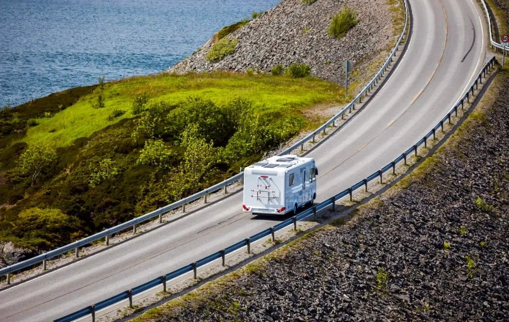 VR circulant sur une route panoramique longeant un plan d’eau, illustrant les longs trajets et les road trips en roulotte.