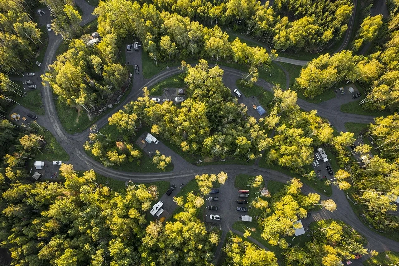 Vue aérienne du camping du parc national de la Pointe-Taillon, montrant les emplacements de VR nichés au cœur d’une forêt dense de feuillus en été.