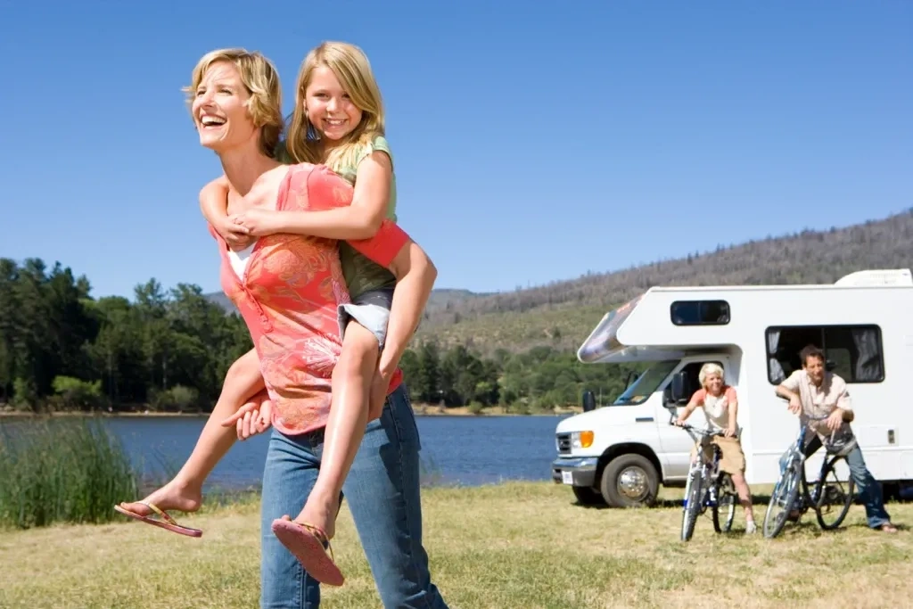 Famille profitant d’activités extérieures près d’un VR stationné au bord d’un lac, illustrant les voyages familiaux en roulotte.