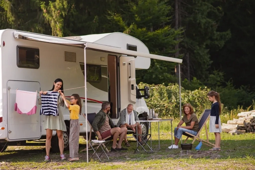 Famille installée devant un VR avec auvent déployé en pleine nature, représentant le confort et la convivialité du camping en roulotte.