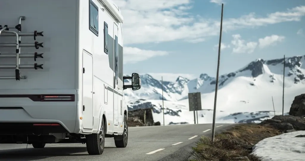 Roulotte circulant sur une route de montagne enneigée, illustrant la préparation hivernale et les avantages d’acheter une roulotte avant la haute saison.
