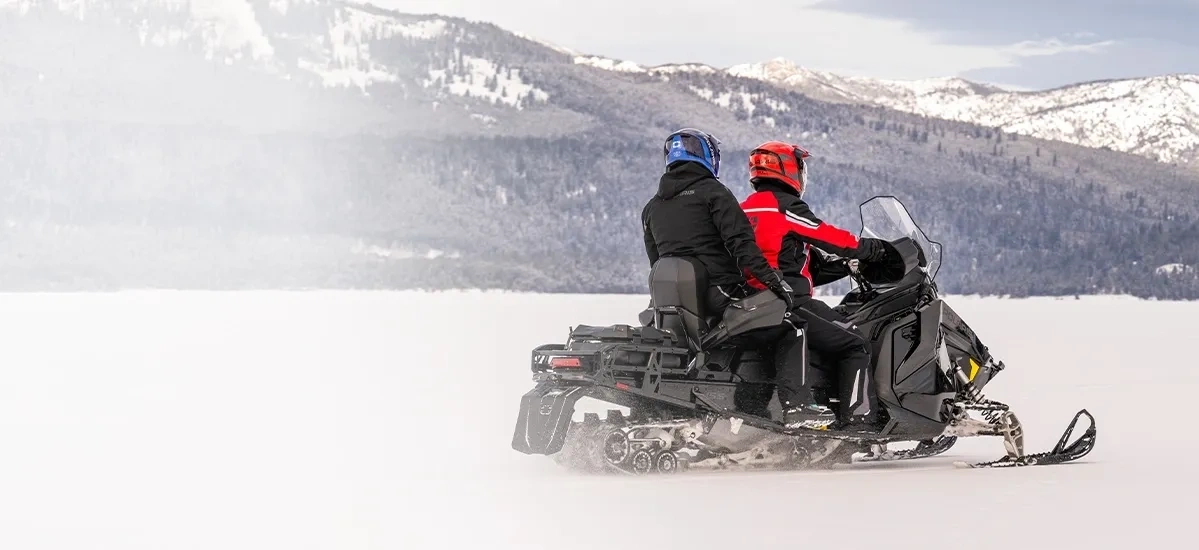 Polaris Voyageur à moteur ProStar S4 transportant deux personnes devant des montagnes enneigées.