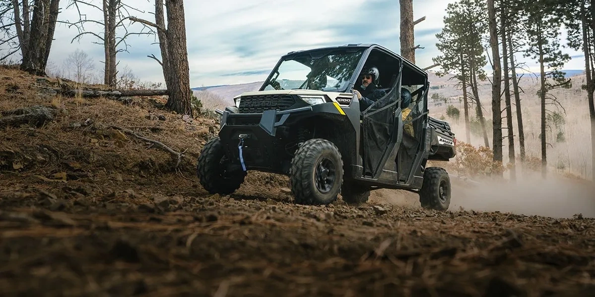 Polaris RANGER 1000 2027 en action sur un chemin de terre accidenté en forêt.