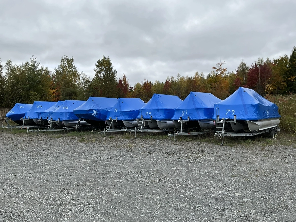 Boats covered with blue protective covers and grouped together in Estrie Marine's storage yard.