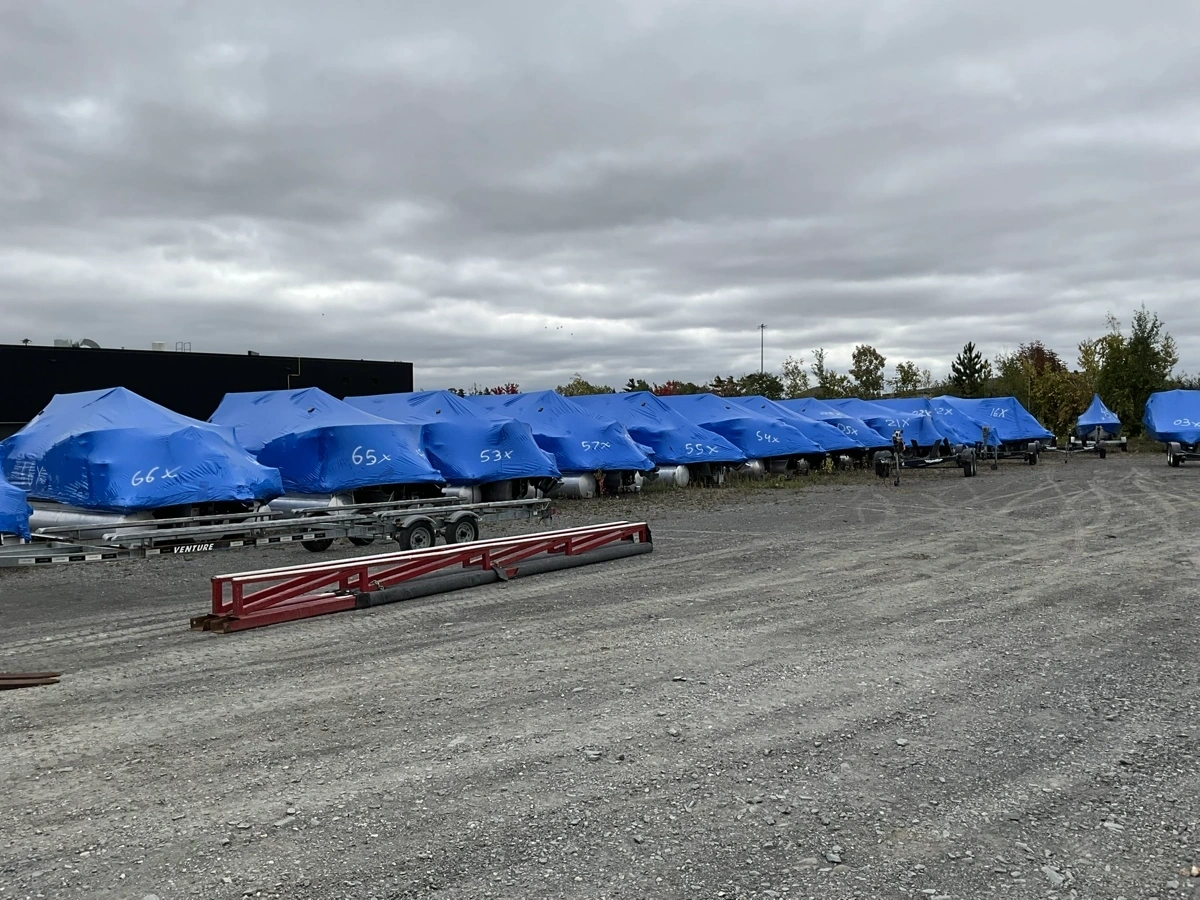 Row of boats on trailers covered with blue protective covers in a storage yard in Sherbrooke.
