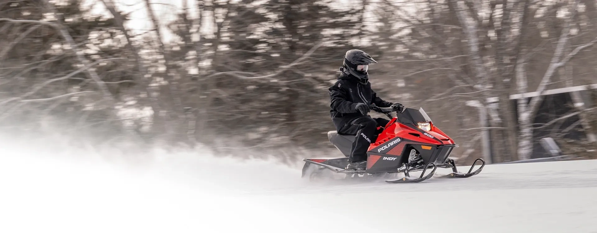 Jeune motoneigiste au guidon d’une Polaris INDY 200 2027 rouge sur un sentier enneigé.