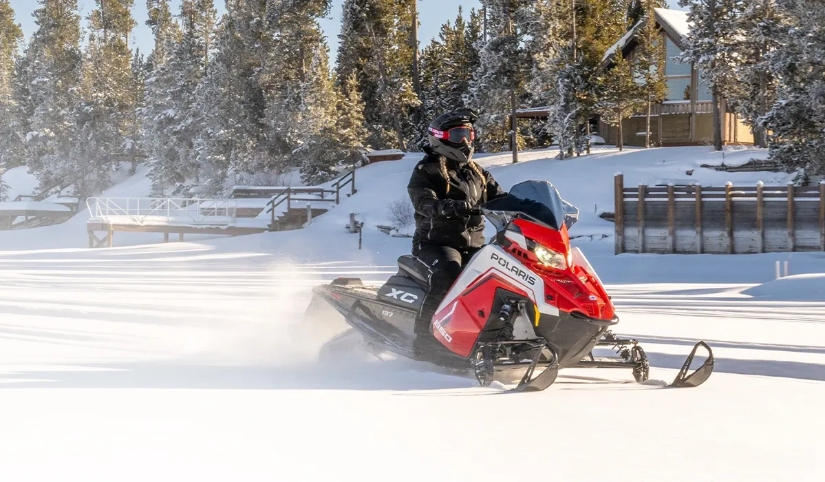 Polaris INDY XC 137 850 2027 rouge en randonnée sur un sentier enneigé bordé de conifères.