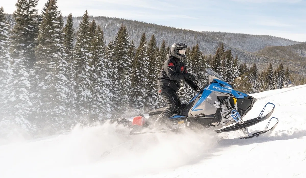 Motoneigiste au guidon d’une Polaris Voyageur Nordic Pro 2027 bleue sur une pente enneigée.