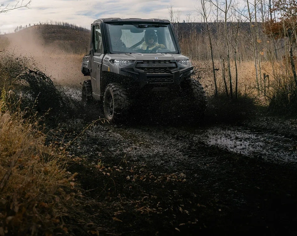 Polaris RANGER XP 1000 CAB 2027 traversant un passage boueux sur un sentier.