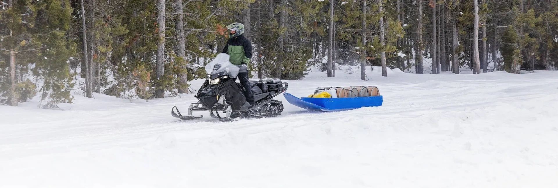 Polaris Voyageur Adventure Ultimate 2027 tirant un traîneau chargé de bois sur un sentier enneigé.