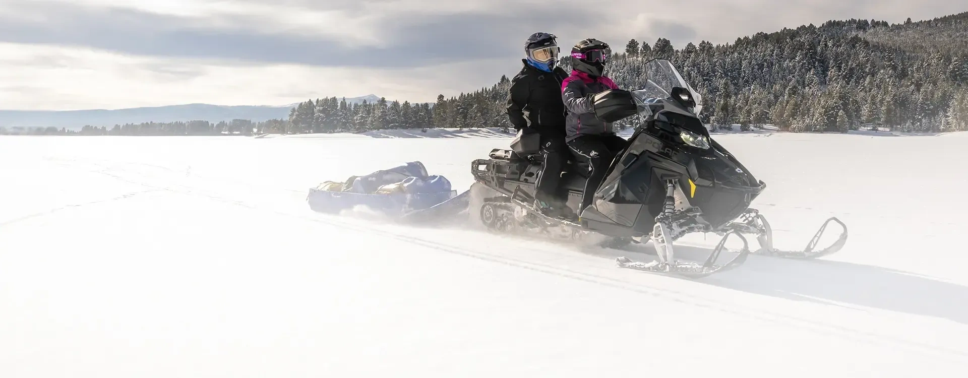 Polaris Voyageur avec conducteur et passager remorquant un traîneau sur une étendue enneigée.