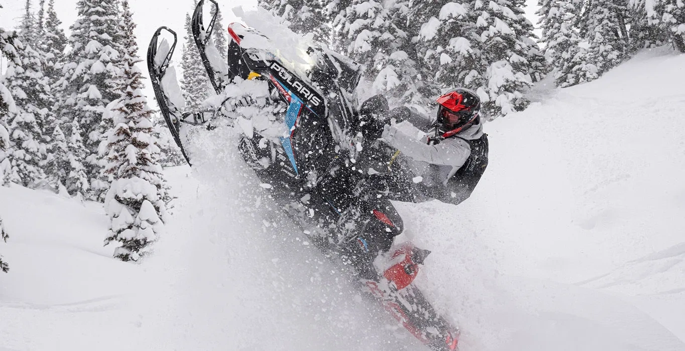 Polaris RMK Factory Edition 155 Patriot 9R 2027 avec les skis soulevés dans la poudreuse en forêt.