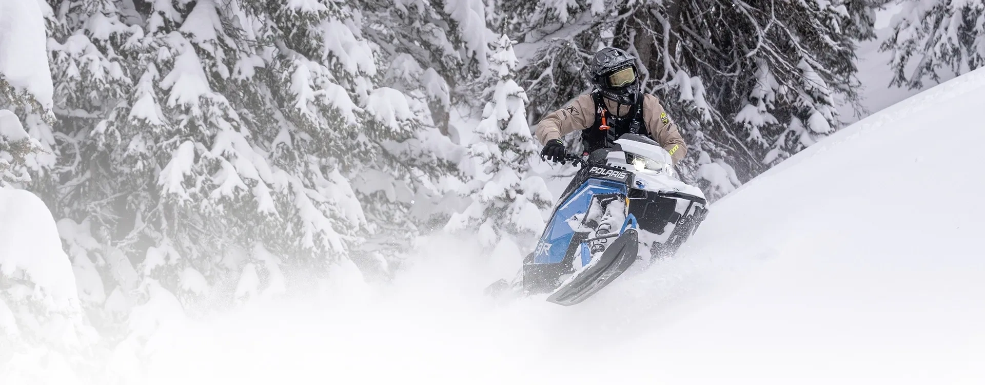 Polaris RMK PRO 2027 en conduite hors-piste dans la neige profonde entre les conifères.