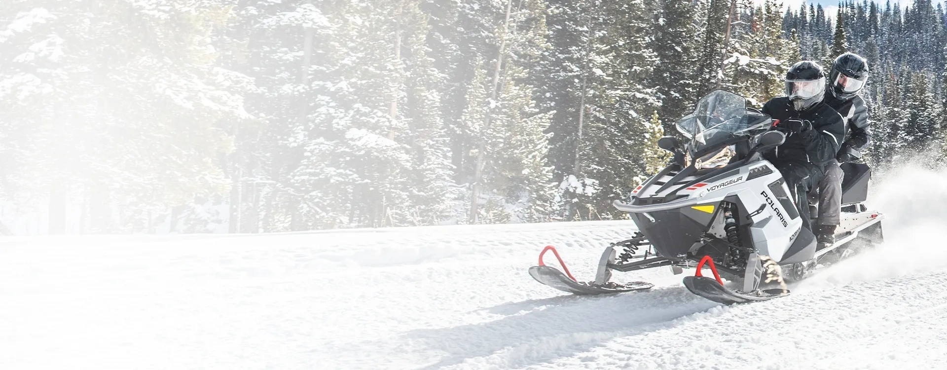 Polaris 550 Voyageur Adventure avec conducteur et passager en randonnée sur un sentier enneigé.