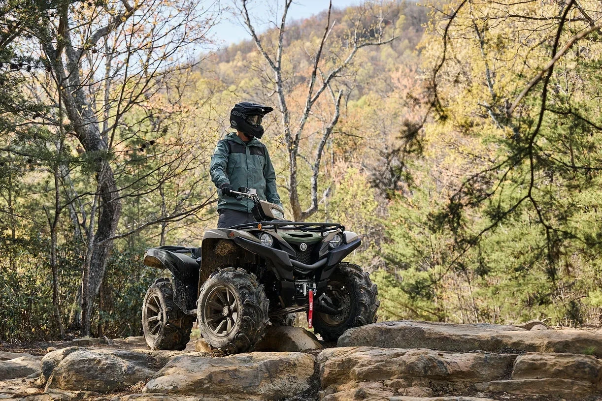 Pilote debout près d'un VTT Yamaha Grizzly EPS XT-R 2027 sur un rocher en forêt.