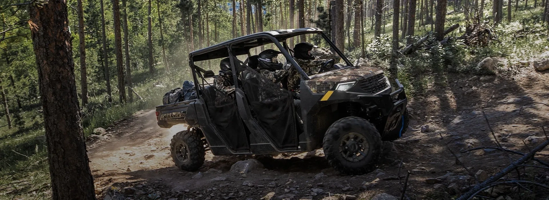 Polaris RANGER 1000 à motif camouflage transportant de l’équipement sur un sentier rocheux en forêt.