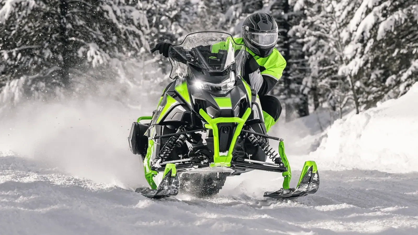 Green 2027 Arctic Cat ZR 600 snowmobile in action on a snowy trail lined with conifers.