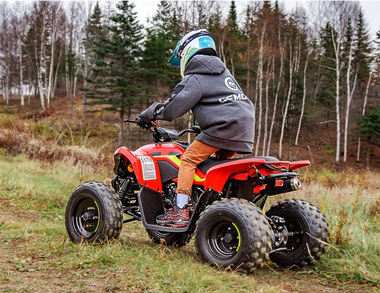 Helmeted rider on a red 2027 CFMOTO CFORCE 110 CLASSIC ATV near a forest.