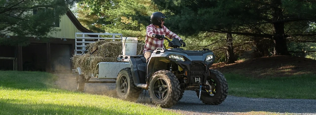Polaris Sportsman 500 2027 remorquant une remorque chargée de foin sur une propriété rurale.