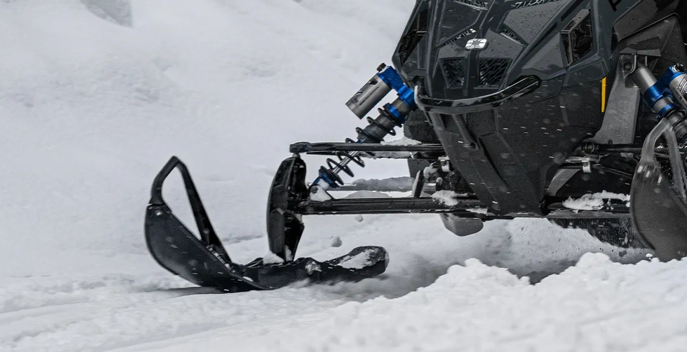 Gros plan sur le ski et la suspension avant d’une motoneige Polaris INDY VR1 9R 2027 dans la neige.