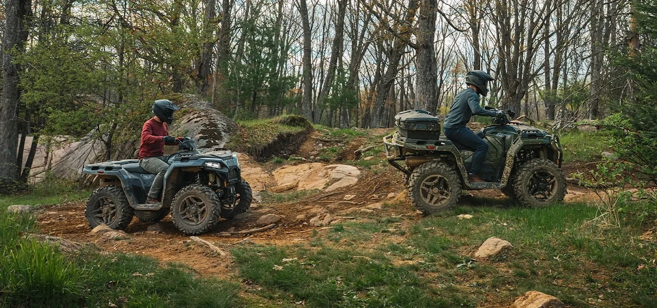 Deux conducteurs en randonnée sur des VTT Polaris Sportsman 500 2027 sur un sentier accidenté en forêt.