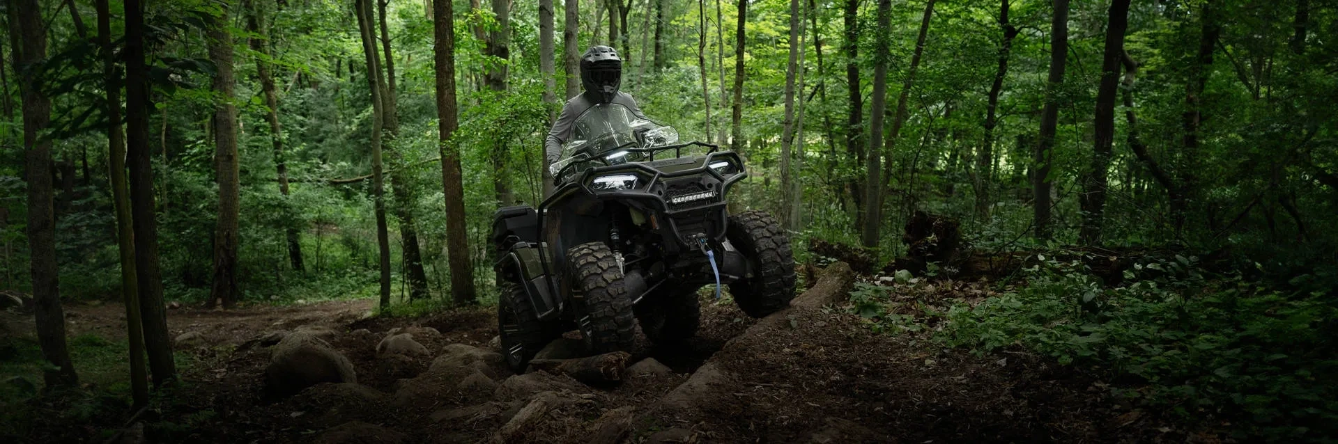 Polaris Sportsman 600 avec son conducteur franchissant des roches sur un sentier forestier.