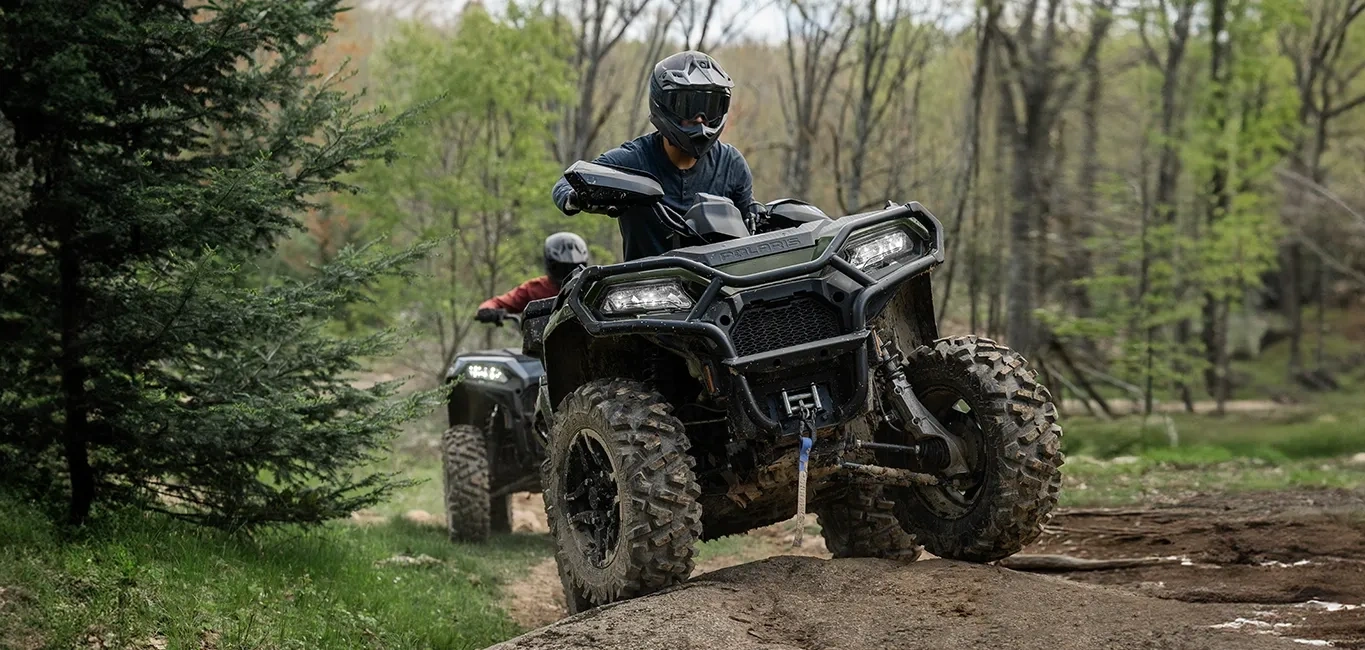 Conducteur au guidon d’un VTT Polaris Sportsman 500 2027 franchissant un obstacle sur un sentier boisé.