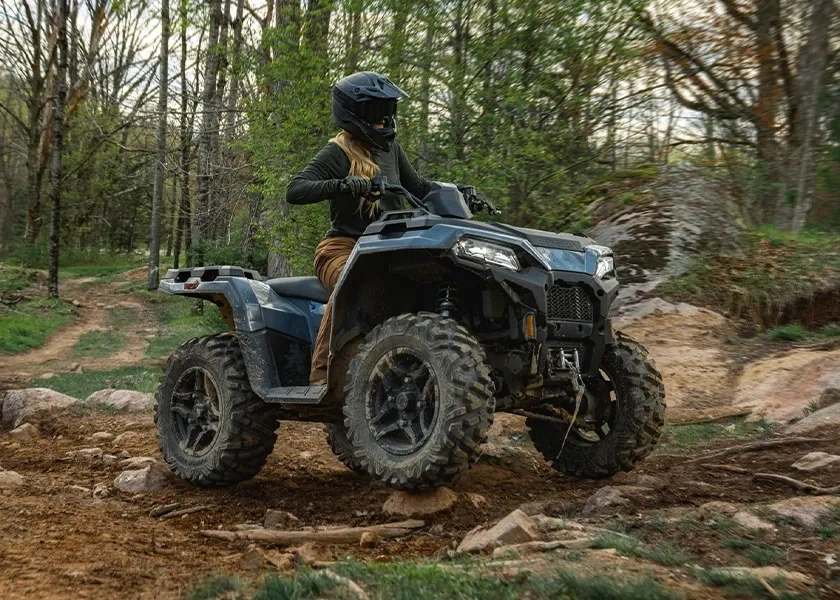 Polaris Sportsman 500 2027 de base avec son conducteur sur un sentier rocheux en forêt.